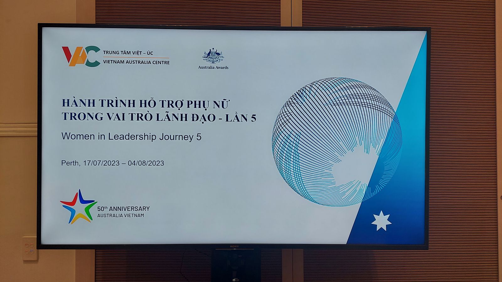 Projected slide image, including the details of the conference. The title 'Women in Leadership Journey 5', first appears in Vietnamese text. Three small logos accompany the text.