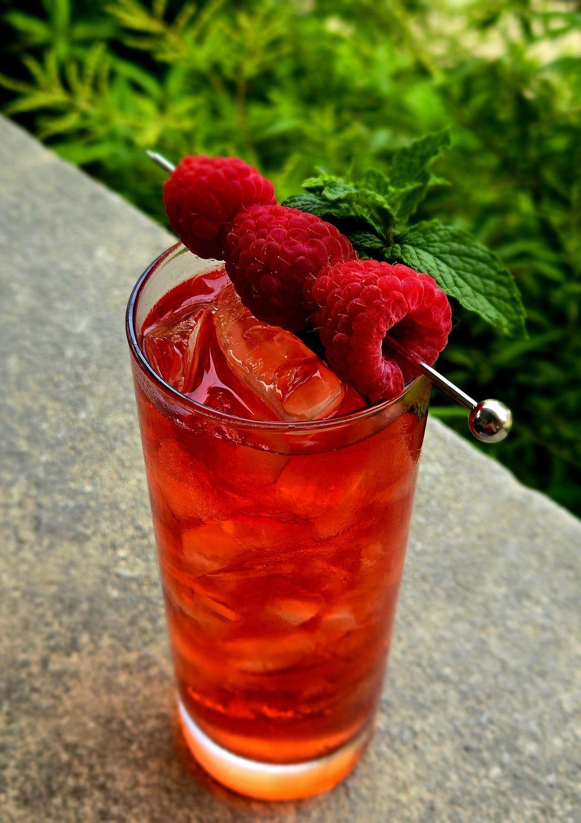 A Raspberry Scotch Whisky Highball with raspberry and mint sprig garnish atop a stone wall.