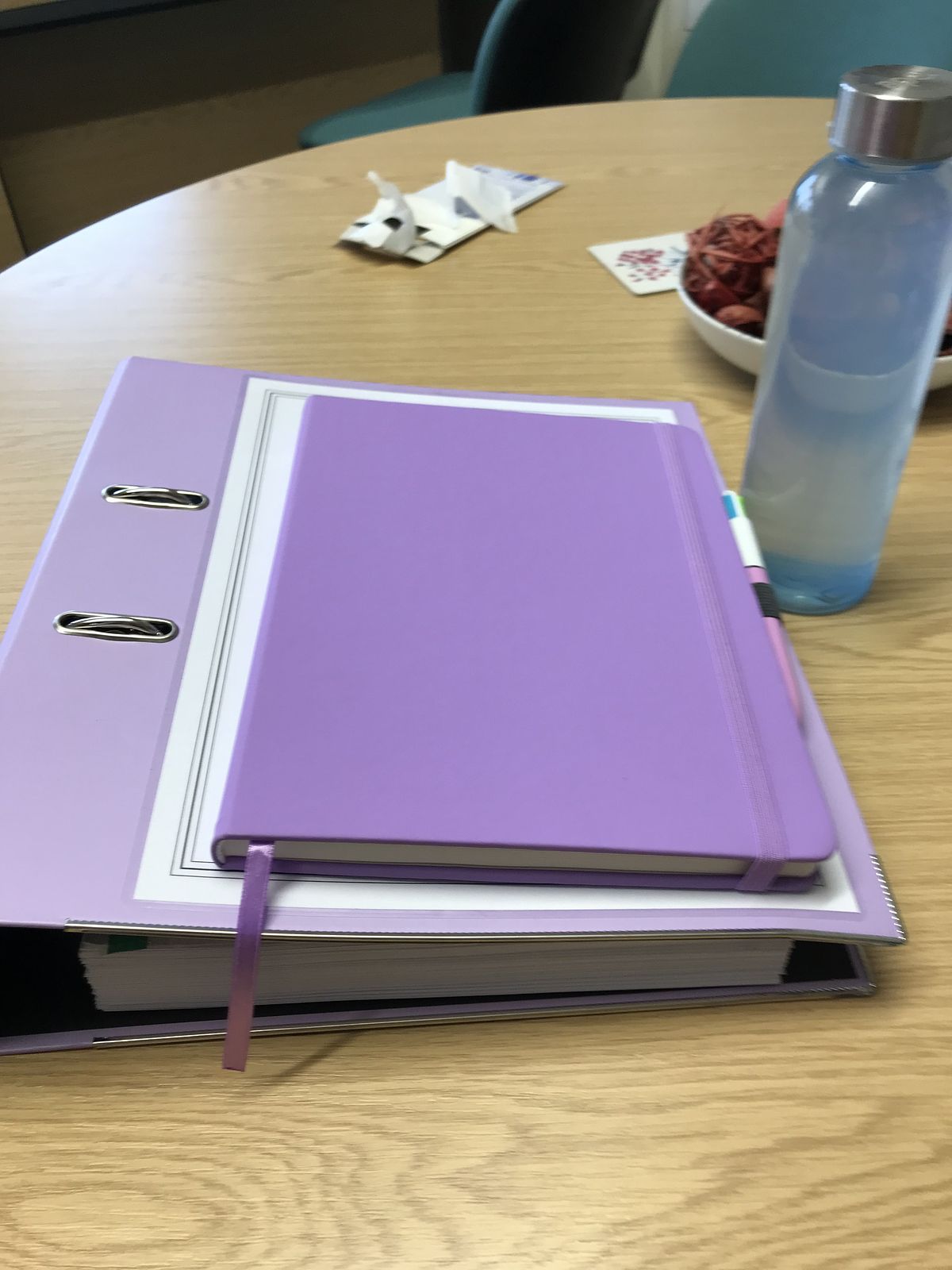 A purple notebook sat on a purple lever arch file with a water bottle standing next to them