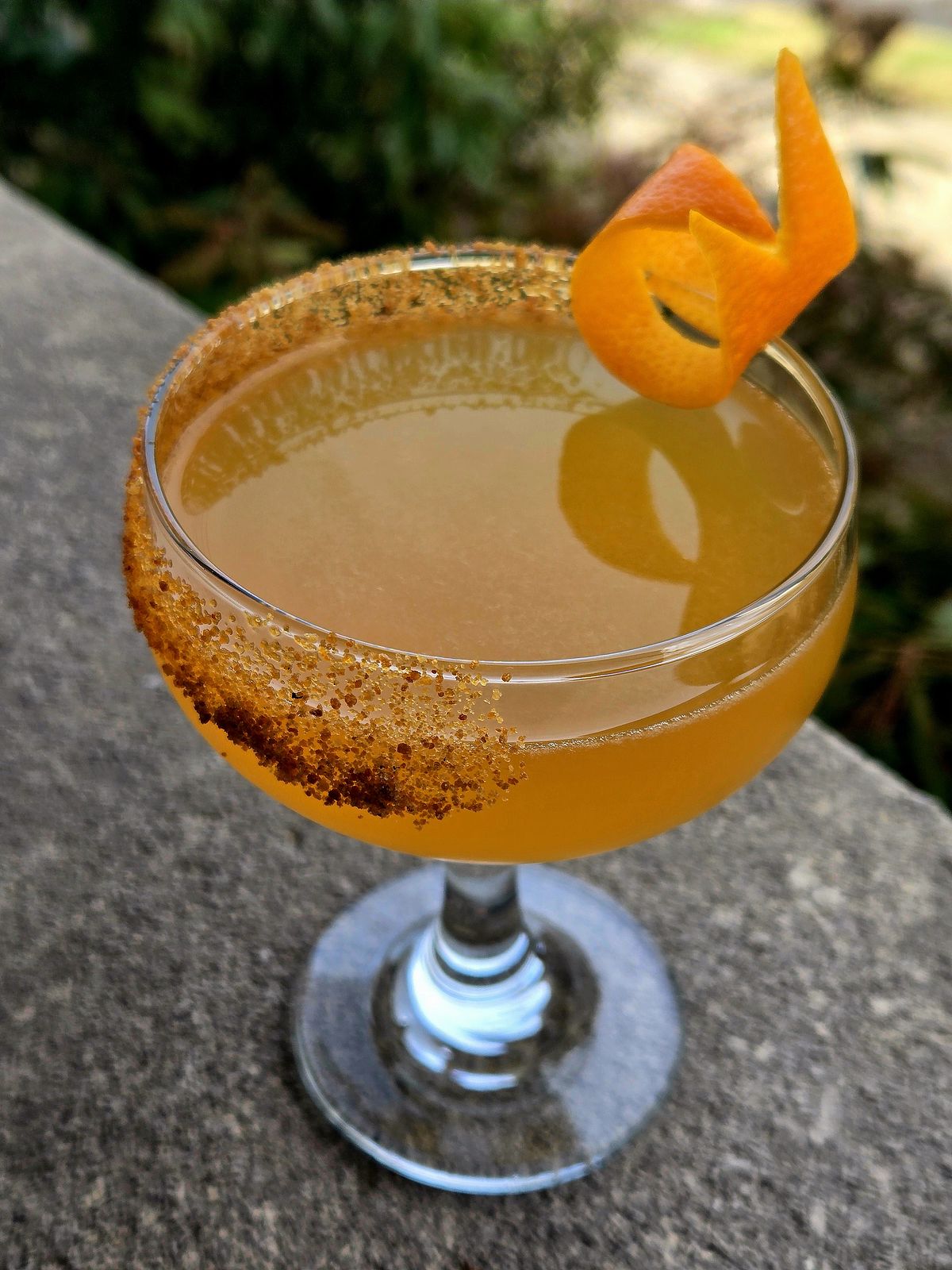 The Sidecar in a Coupe with orange twist and coconunt sugar rim atop a stone wall.
