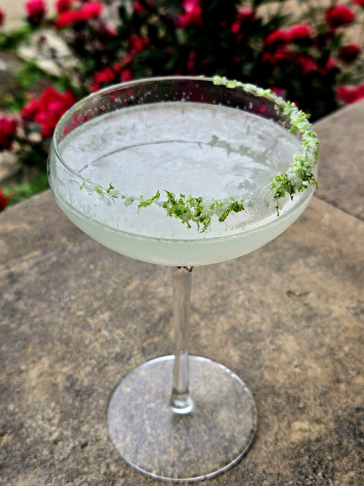 Coconut Margarita with Triple Sec and lime salt rim in a Coupe atop a stone wall.