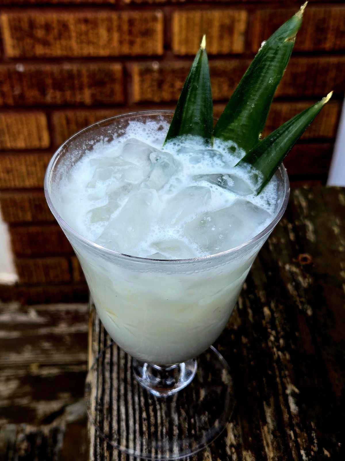 White Cloud rum cocktail with pineapple frond garnish in a vintage wine glass atop a wooden step.